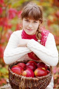 微笑的少女抱着篮子苹果在秋天的花园里