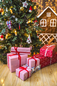 包装礼品的红色和白色的包装下的绿色圣诞树装饰圣诞玩具和蜡烛。背景是姜饼屋和黄色圣诞灯