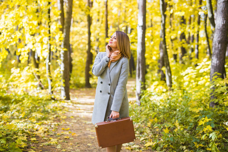 季节, 自然和人概念妇女在秋天公园与手提箱一起摆姿势