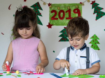 可爱的孩子们从事创造力。微笑滑稽的孩子制作圣诞卡。圣诞节和2019新年概念