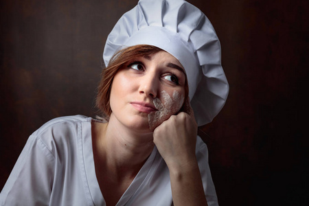 疲倦的年轻美丽的女孩在一个棕色背景的厨师制服