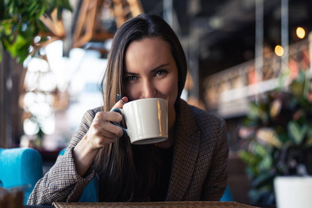 一个年轻的企业妇女的肖像喝茶从一杯特写与模糊的餐厅背景