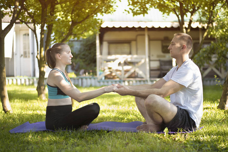 一对恋人坐在地毯上做瑜伽, 牵着手。早晨在夏天庭院里