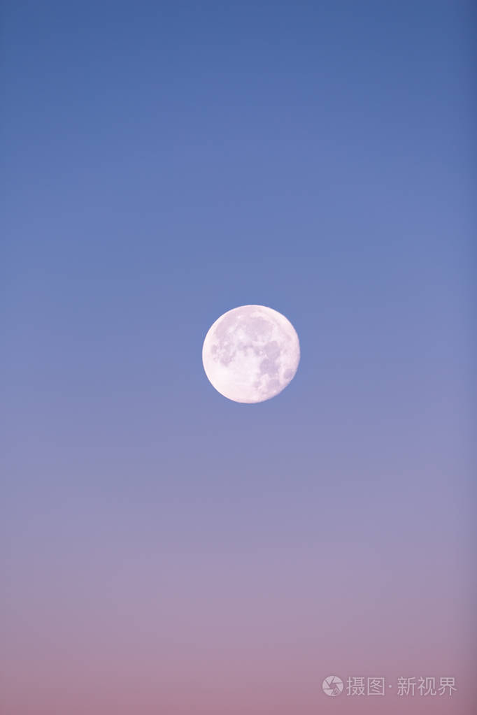 近满月在柔和的粉红色和蓝色的冬天天空升起