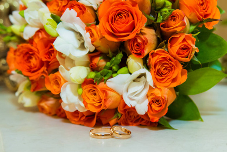 结婚戒指两个金色的复古戒指和一束橙色玫瑰和白色花朵的新娘花束