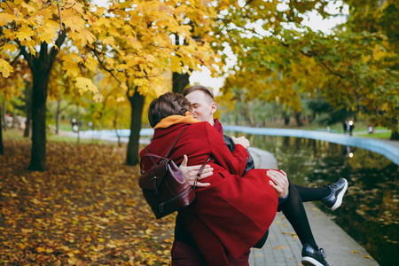 年轻幸福美丽的情侣在爱英俊的男子抱着女人拥抱拥抱亲吻在秋天的城市公园户外散步附近的水。恋爱关系家庭人生活方式概念