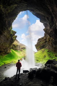 Kvernufoss 瀑布在山的峡谷。旅游胜地冰岛。穿着红色夹克的男子站着, 看着流水。自然美