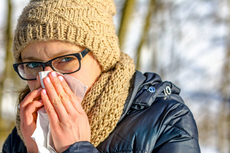 冷鼻子的女人在纸巾里吹。秋季生病或感冒和流感的人, 户外