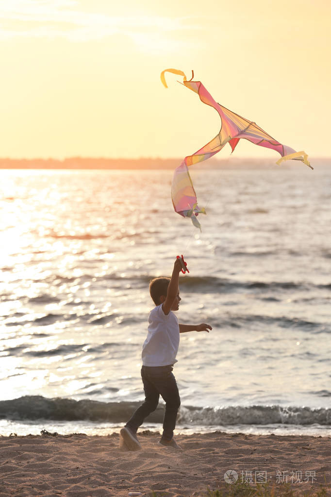 可爱的小男孩在日落时在河边放飞风筝