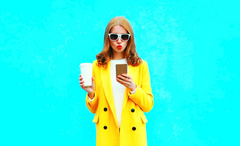 时尚肖像女人使用智能手机持有彩色蓝色背景杯咖啡