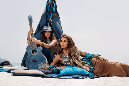 用吉他坐在枕头在山丘上的两个美丽的吉普赛女孩