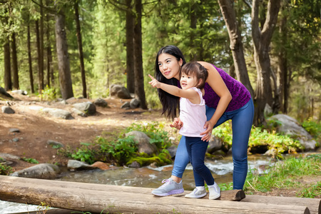 亚裔女子和她的小女儿河站在日志上附近的树林中
