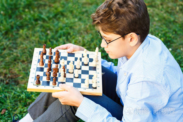 可爱的小男孩穿着蓝色衬衣, 在夏天, 圆眼镜在公园里下棋.