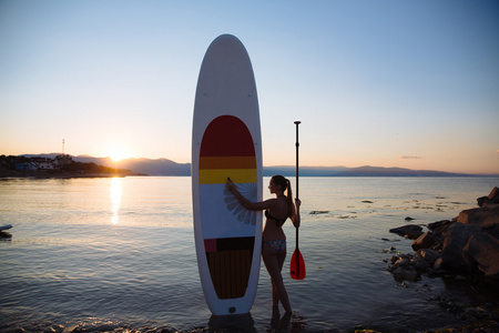 年轻女孩与 sup 冲浪和桨在海洋的轮廓。概念的生活方式 体育 爱