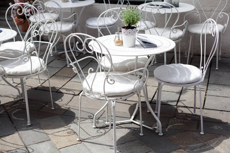 在阳光明媚的夏日, 有美丽的白色锻铁椅和桌子的咖啡馆的室外露台