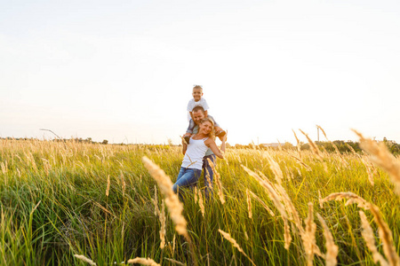 年轻的家庭与儿子散步和有良好的时间在绿色田野在日落