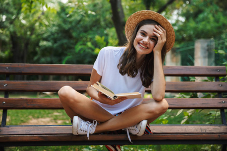 愉快的女孩读一本书, 而坐在公园户外