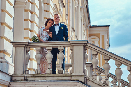 在美丽的老宫殿的台阶上摆姿势的幸福新婚夫妇的全身肖像