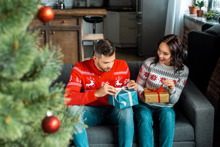 夫妇坐在沙发上的选择焦点家庭圣诞树附近的礼品盒