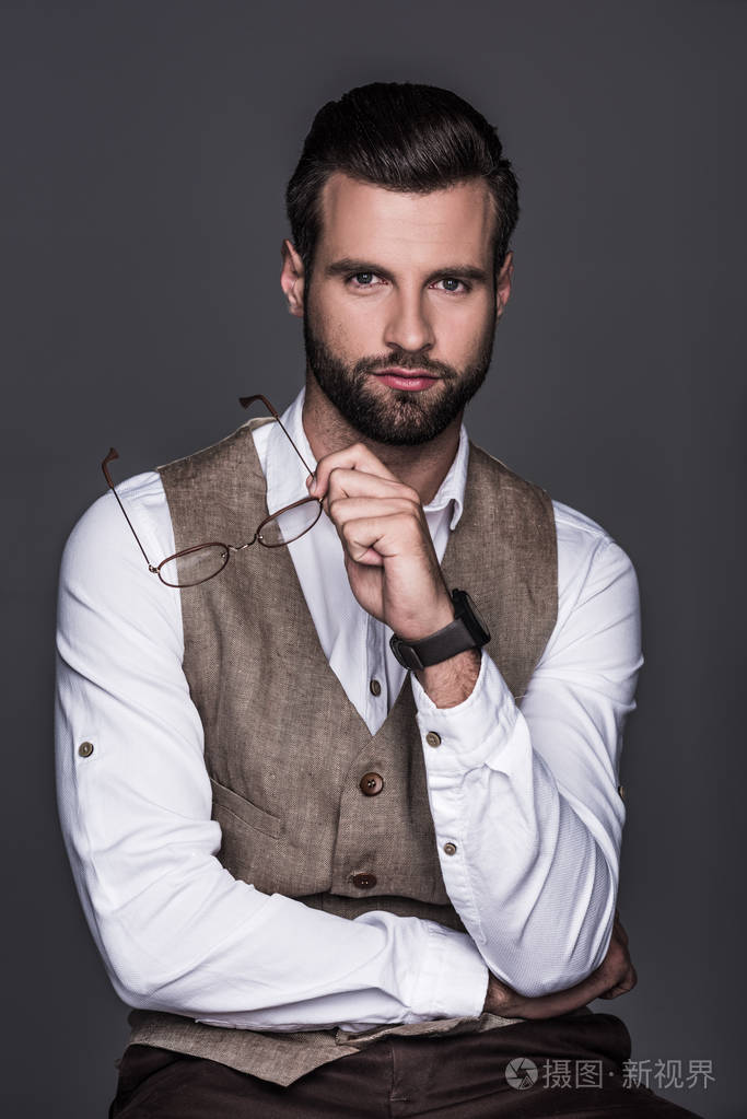 时尚男子的肖像手持眼镜和摆在优雅的背心, 孤立的灰色