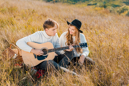 年轻男吉他,而女人在草地上微笑