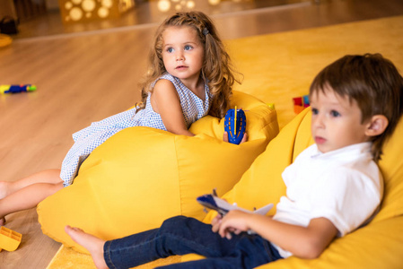 可爱的孩子, 玩具躺在黄色的豆子袋椅上幼儿园, 看着远离