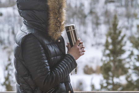 冬天穿着冬天夹克的女孩, 手里拿着一壶咖啡或茶在阳台上