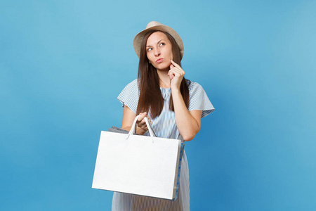 肖像沉思美丽的白种女人在夏天的礼服, 草帽向上看, 拿着包袋与购买后, 在蓝色粉彩背景的购物隔离。复制广告空间