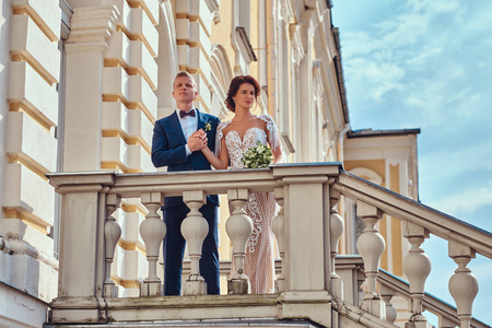 幸福的新婚夫妇的肖像在美丽的老宫殿的楼梯上摆姿势时拥抱