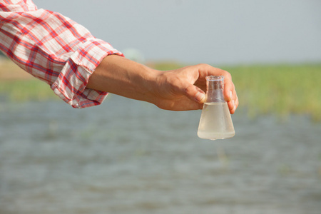 水纯度测试手拿着化学瓶与液体 湖泊或河流中背景