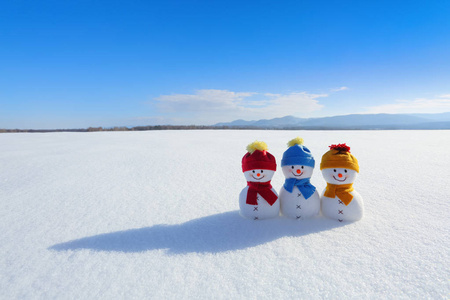 三人在五颜六色的帽子站立在雪。风景与山, 田野在雪, 蓝天。美丽的冬日