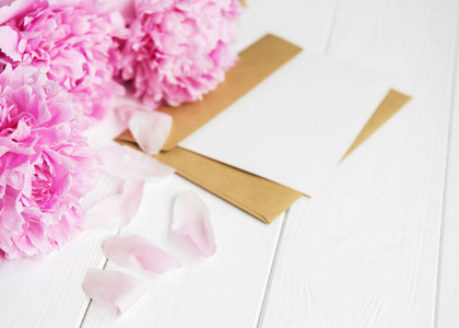 一张白色木桌上的请柬工艺信封和粉红色牡丹花