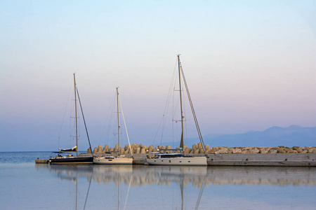 停泊在 Ereikoussa 港的豪华游艇反映在平静的水中。美丽的日出在海在风景如画的地中海 Ereikoussa 海岛在希腊