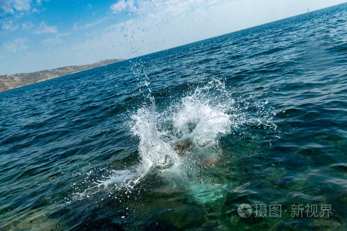 一个男孩正从悬崖上跳到海里, 在炎热的夏日里溅起了大水花.