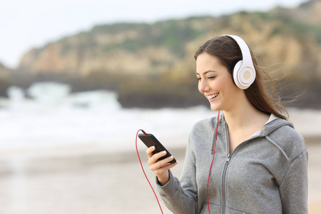 快乐的十几岁的女孩听音乐与耳机和一个智能手机在海滩上
