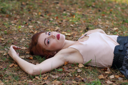 美丽的女孩穿着短裙带位于干树叶在秋天