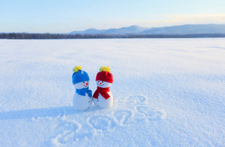 快乐的一对雪人在爱情中站在雪地上。蓝色的红色帽子和围巾。文字2020。寒冷冬日里的山水