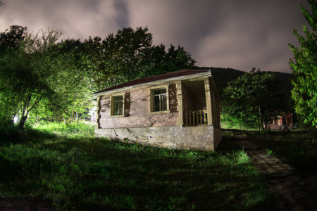 晚上在森林里建筑的山夜风景与月亮或老式乡下房子在晚上与云彩和星.