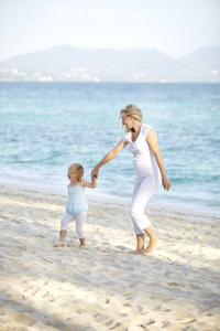 年轻孕妇与女儿在沙滩上散步