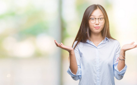年轻的亚洲商业妇女戴着眼镜, 在孤立的背景下无能和混淆表达与胳膊和手提出。怀疑概念