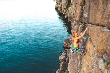 水上的登山者。一个女人爬上岩石。自然地形的训练。极限运动。海滨登山路线