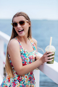 美丽的年轻女子带着太阳眼镜喝绿色蔬菜思慕雪