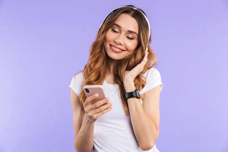 一个微笑的年轻女孩的肖像手持手机在紫罗兰色背景下, 听音乐与耳机