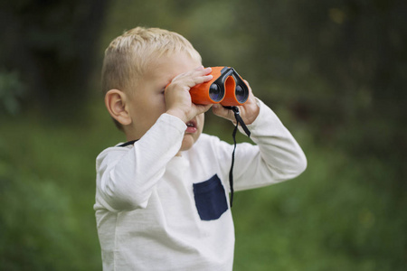 小男孩年轻研究员在阳光明媚的日子, 在绿色森林中探索望远镜环境
