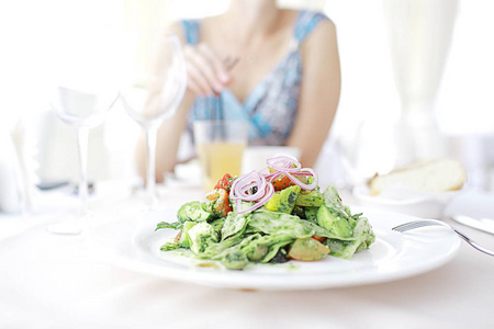 美味的绿色沙拉，在一家咖啡馆，坐在背景的年轻女人