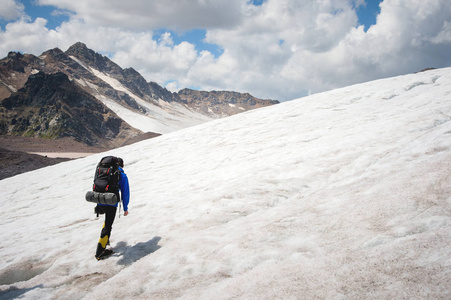 有背包的登山运动员在冰镐漫步在布满灰尘的冰川上, 手里有人行道在山上的裂缝之间。