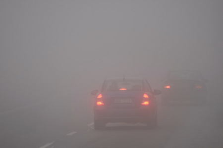 在雾中的汽车。恶劣的冬季天气和危险的汽车交通的道路上。轻型车辆在雾中