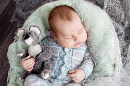 可爱的新生宝宝睡在篮子里。美丽的新生男孩与熊玩具