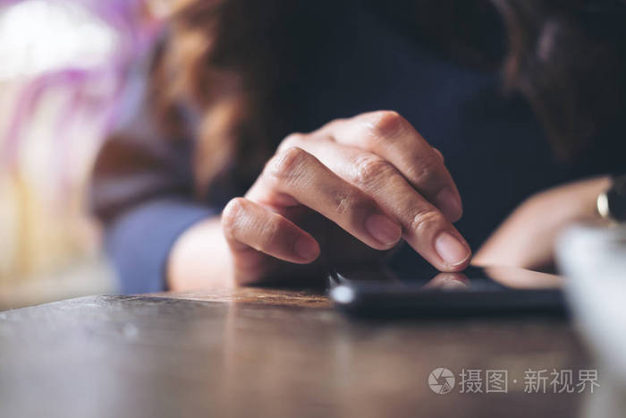 在现代咖啡馆的木桌上的一个黑色智能手机上, 一个商业女性的手摸和