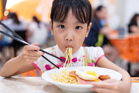 亚洲华人小女孩在餐厅用筷子吃面条